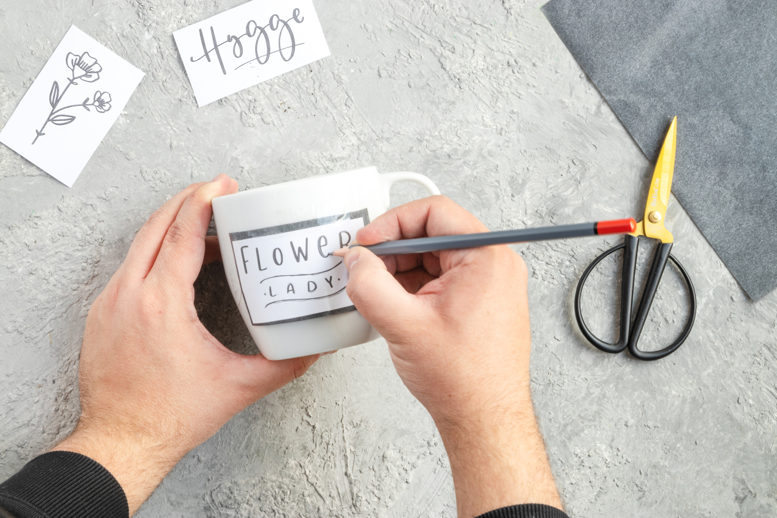 Das Motiv zum DIY-Blumengeschenk von Pink Kisses wird mit einem Bleistift und Kohlepapier auf die Tasse übertragen